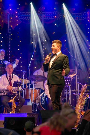 Dylan singing in a tuxedo under stage spotlights with a big band