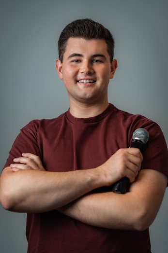 Dylan smiling with arms crossed, holding a microphone