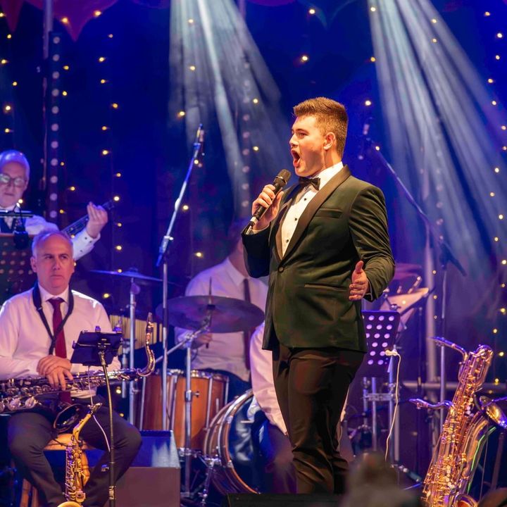 Dylan Forge in a green velvet jacket singing with a big band at a Christmas concert