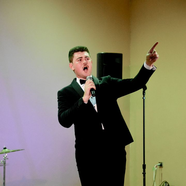 Dylan Forge in a tuxedo, singing and pointing to the audience