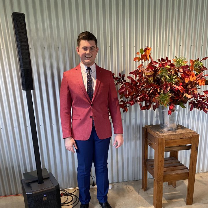 Dylan Forge in a red blazer beside his battery-powered PA system