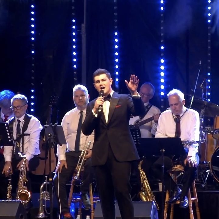 Dylan Forge singing with a big band under blue stage lights