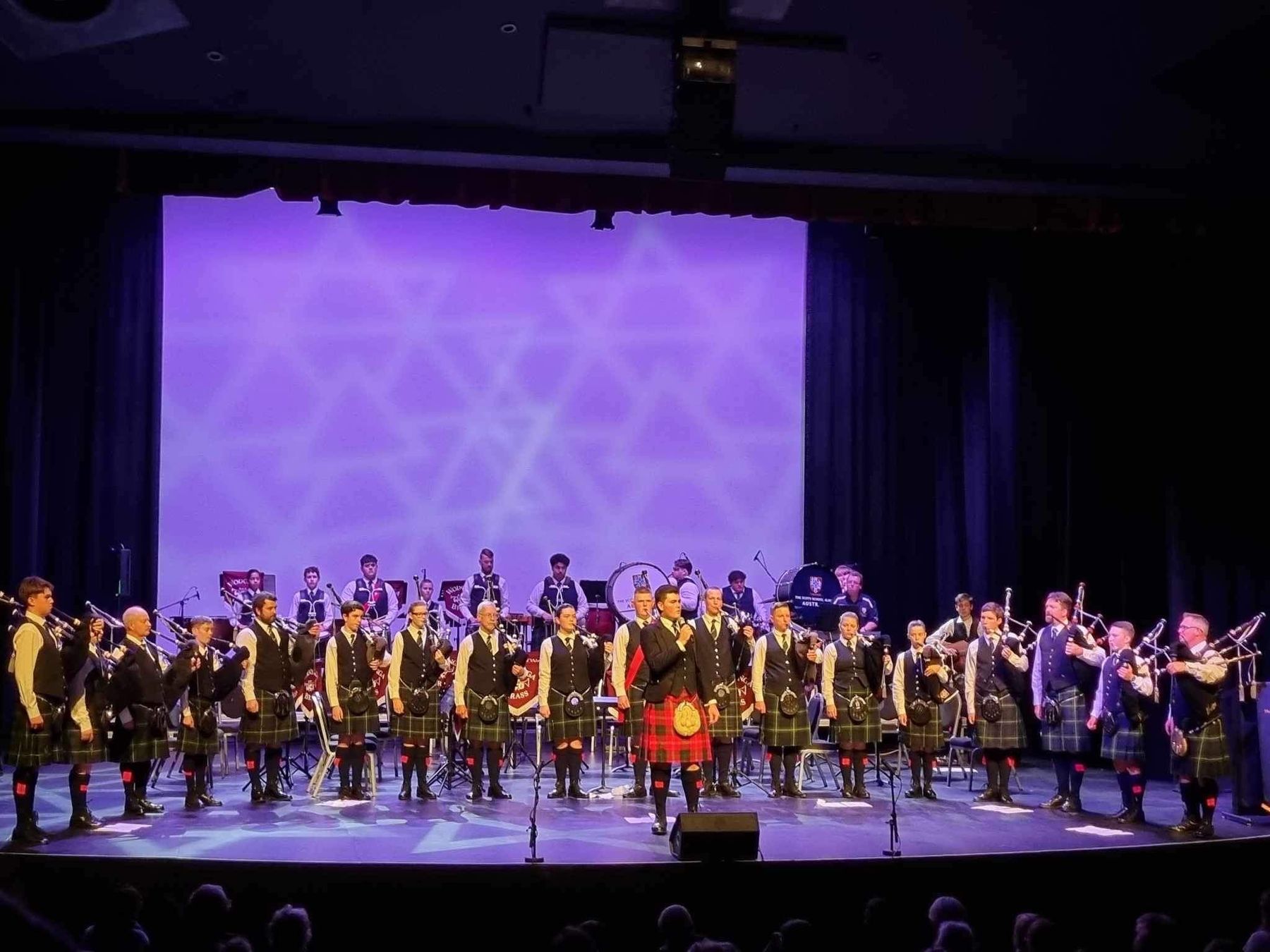 Dylan Forge on a theatre stage with a pipe band